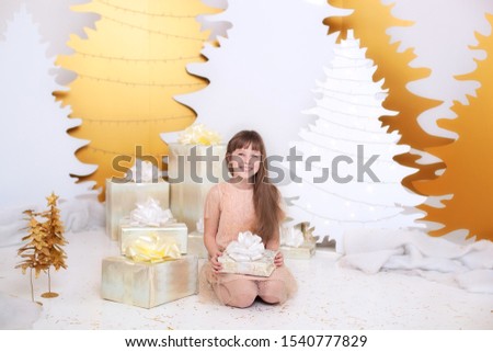 young girl in golden dress laughs and enjoys gift. Little girl opening magical christmas present at home. child holds christmas present. Merry Christmas and happy holidays. New Year. Xmas interior 