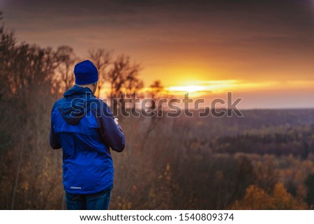Man in blue taking pictures with a phone of a beautiful sunset.