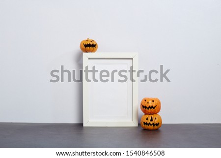 Mock up black frame with Jack o Lantern and pumpkin decor on a shelf or desk. 2020 Halloween concept. Portrait frame against a white wall, cop