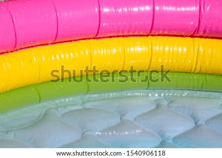 Bright blue inflatable paddling pool surface with water ripples. Summer picture of swimming pool with green, yellow and pink side. Background or backdrop