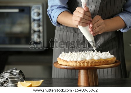 Woman preparing lemon meringue pie at table in kitchen, closeup