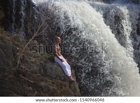 a man meditates on the background of a waterfall, on the banks of the river, a Buddhist monk, fellowship with god