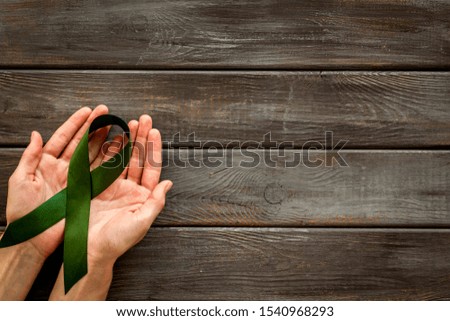 Jade ribbon in hands as symbol of disease control on dark wooden background top view space for text