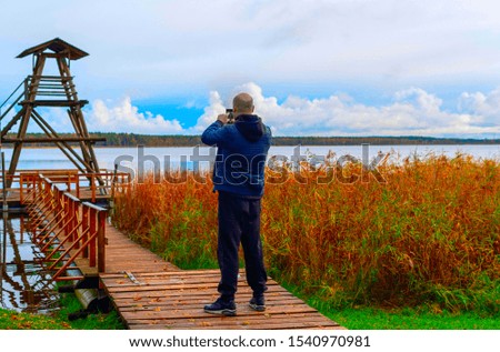 a man takes a photo of bird watching tower on the lake. reflection of the sky in the water. the concept of calmness and relaxation