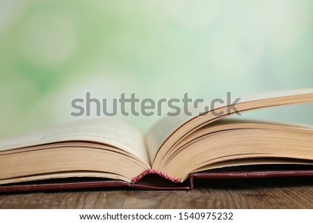 Open book on wooden table against blurred green background, closeup. Space for text