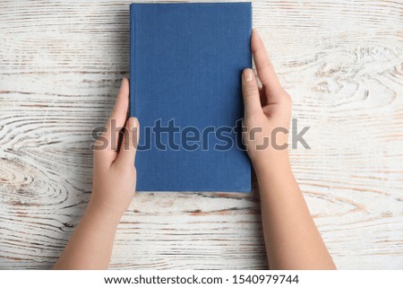 Woman holding hardcover book on white wooden background, top view