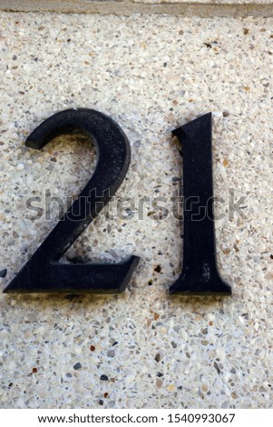 Number 21. Metal figures on white stone wall. Street number.