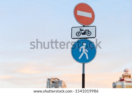 no entry road sign with a motorcycle sign along with a pedestrian zone road sign against a blue sky and tops of high-rise apartment buildings