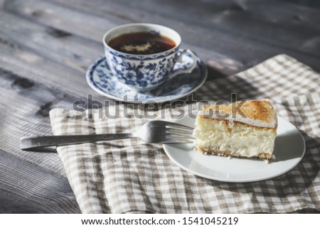 On a dark countertop, on a light checkered linen napkin, a white and blue patterned tea pair with tea and saucer with a piece of classic cheesecake and a fork
Close-up of a piece of classic cheesecake