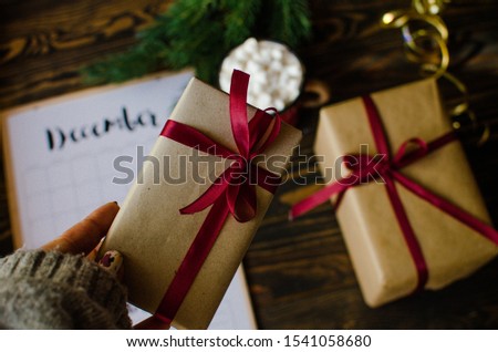 Woman giving a Christmas gift wrapped in red paper and white ribbon on a wooden table - top view, panoramic web banner with copy space