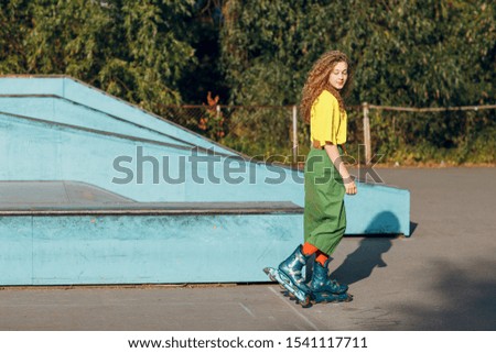 Young woman girl in green and yellow clothes and orange stockings with curly hairstyle roller skating in skate park