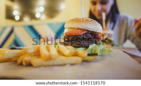 A big juicy burger with two cutlets, vegetables, sauce and french fries on the table in a cafe.