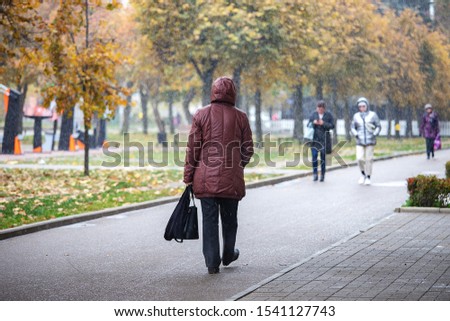 the change of weather during the late autumn, a cold snap and the first snowstorm on the streets of the city makes people hide their heads under a hood and a hat from the snowfall Royalty-Free Stock Photo #1541127743