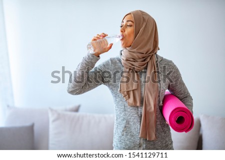 Young muslim woman ready to running. Islamic woman resting and drinking water after fitness workout. Healthy sporty woman in hijab ready to yoga class. 