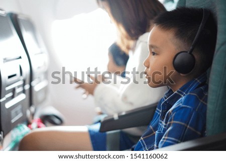 An Asian boy is watching the screen in an airplane.