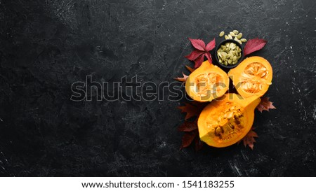 Autumn vegetables. Pumpkin with pumpkin seeds and autumn leaves. flat lay. On a black stone background. Top view. Free space for your text.