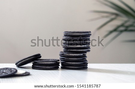 black cookies standing pinnacle with white cream center on a white wooden background with palm leaves behind.