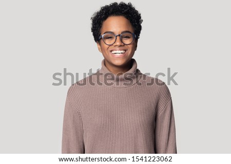 Head shot portrait close up smiling African American girl wearing glasses and sweater looking at camera, excited beautiful girl laughing, having fun, standing isolated on grey background