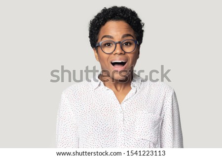 Head shot portrait close up excited African American woman in glasses with open mouth looking at camera, unexpected good news, great shopping discount offer, isolated on grey background