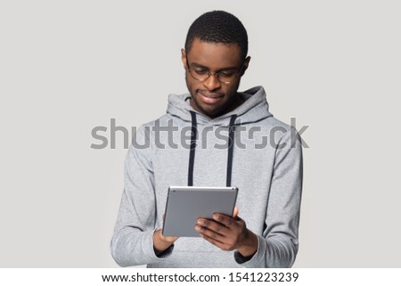Head shot close up African American man in glasses using computer tablet, looking at screen, isolated on grey background, young male using electronic device, reading book or news in social network