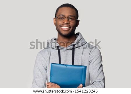 Head shot portrait smiling African American man in glasses holding folder for papers with documents, happy handsome student, worker looking at camera, posing for photo isolated on grey background