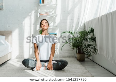 beautiful happy girl with closed eyes practicing yoga in lotus position in bedroom in the morning  Royalty-Free Stock Photo #1541237930