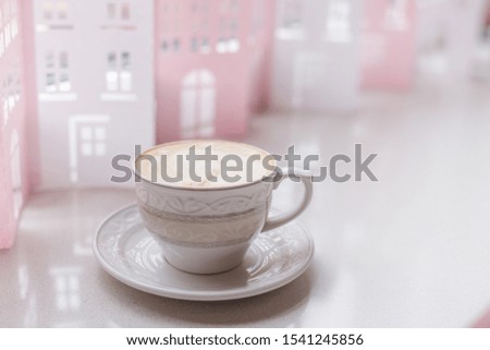A beautiful white cup and saucer, filled with cappuccino, stands against the backdrop of white and pink house decorations, a place for text, a horizontal banner