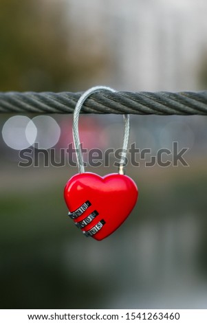 Red padlock on a rope, bokeh of evening city lights. Symbol of love. Romantic concept. Metal heart on a cable on river bridge. Heart hanging on clothesline. 