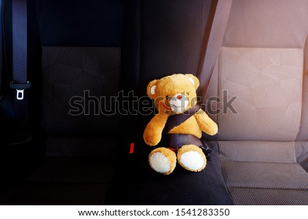 The picture of a teddy bear is fastened with a seat belt in the car to show the safety of children using the car.