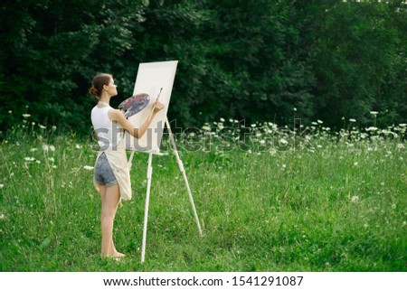young slender woman in a forest glade girl draws on canvas