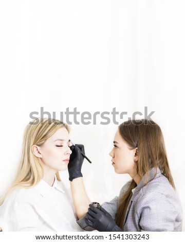 Female cosmetologist performs eyebrow correction on beautiful models in the beauty parlor. The girl's face is a blonde. Close-up. Facial care.