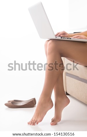 Beautiful legs. Cropped image of beautiful female legs with laptop on top isolated on white