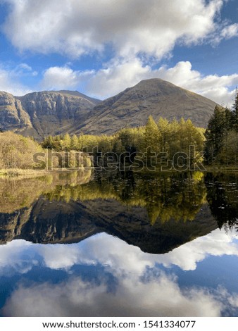 Autumn coloured trees and mountains reflecting on a calm Lochan, from Glencoe in the Scottish Highlands