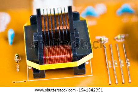 Magnetic ferrite core transformer detail on beige printed circuit board. Close-up of induction coils with copper wire winding. Electronic components in electrotechnics. Disassembled electrical device. Royalty-Free Stock Photo #1541342951
