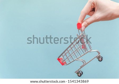 woman's hand holds a shopping cart on a blue background close-up. Copy space