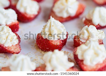 Stuffed strawberries filled with cheesecake filling made with whipped cream and cream cheese. Sprinkled with graham cracker crumbs. Selective focus with blurred foreground and background.