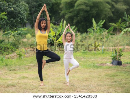 Mother and daughter asia doing yoga Tree pose at park