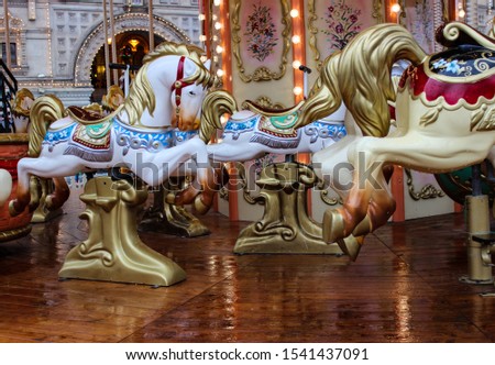 The two-story carousel. Big, beautiful with white horses. A lot of fairy lights and decorative items with monograms. Fenced with a small fence. The wooden floor is wet from the rain.