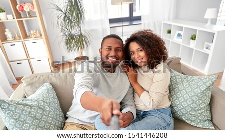 family, technology and people concept - happy african american couple taking picture selfie stick at home