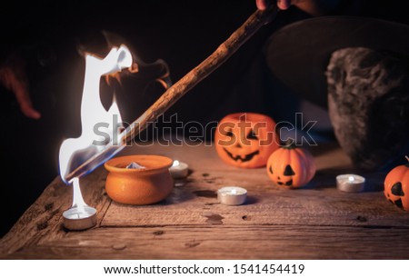 Witch doing curse and ceremony in the dark of Halloween night on the table with candles, skull and wand. Picture is partly focused.
