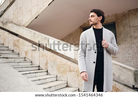 Young attractive stylish man in coat thoughtfully looking away on street