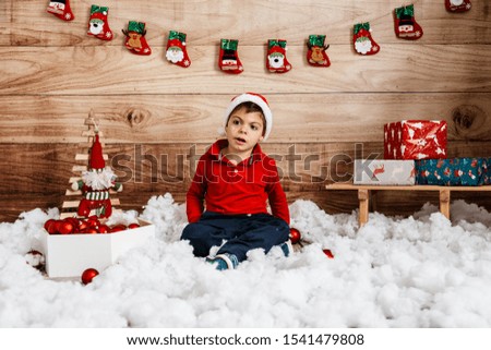 Christmas photo session of a four-year-old child with multiple disabilities. session in a photo studio in rustic style. wooden background, with sled, red suit, gifts, hanging socks, santa claus