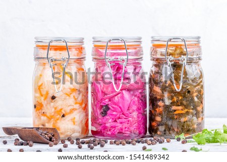 Fermented preserved vegetarian food. Homemade marinated cabbage kimchi, sea kale with carrot, sauerkraut sour in glass jars on rustic wooden kitchen table. Canned vegetables food concept Royalty-Free Stock Photo #1541489342