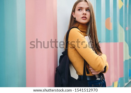 Beautiful pensive student girl with laptop thoughtfully looking away over colorful background outdoor