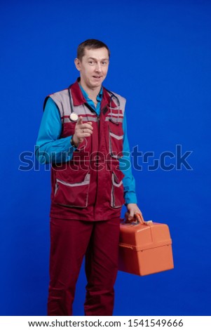 Ambulance doctor man in a work suit and with a box in his hands posing on a blue background