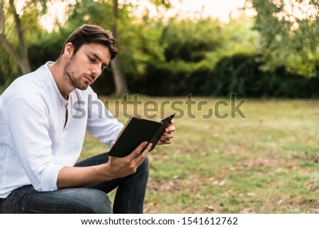 Young man sitting in a park carefully reads an old book.