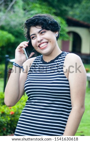 Relaxed and smiling young woman dressed in a striped dress, talking on her smart phone. Concept of feminine beauty. Colorful photo