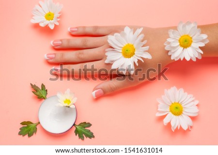 Female hand and cosmetic cream on a pink background among flowers. View from top. Flat lay photo with place for text.