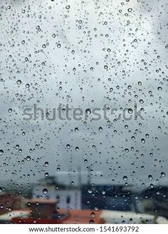 Big drops of rain on the window glass, during the storm. View of the overcast clouds and green trees and buildings. Urban view of rain drops falls on a window during a stormy day. Rain drop on window 