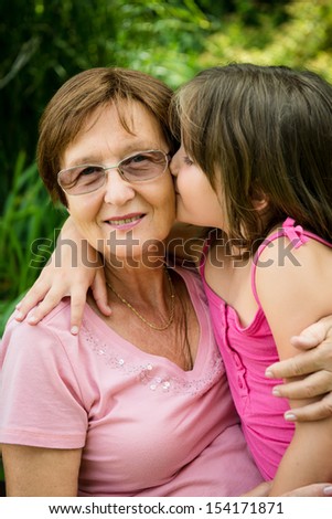 Lifestyle portrait of grandchild kissing grandmother - outdoor in nature